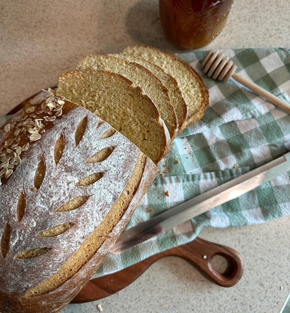 loaf of bread laying on a towel beside bread knife, jar of honey, and honey scoop