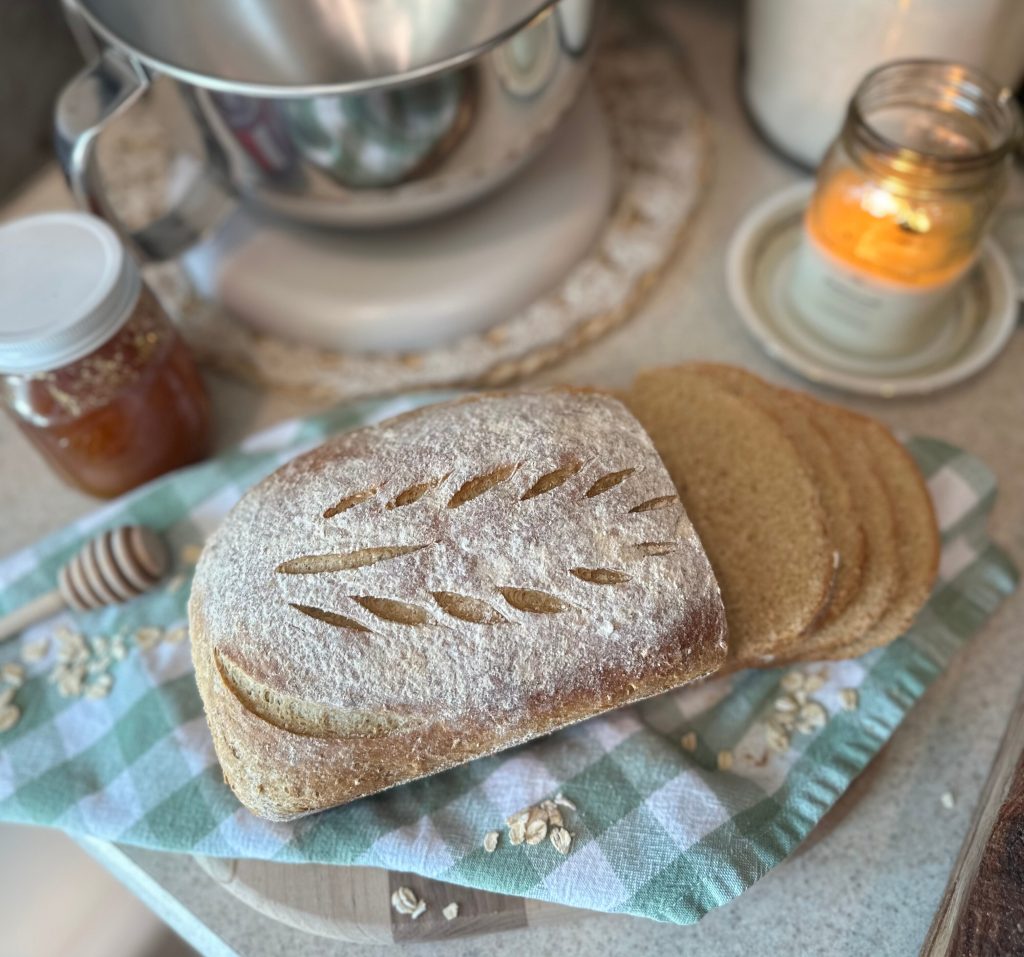 loaf of bread on tea towel beside lit candle, jar of honey, and stand mixer