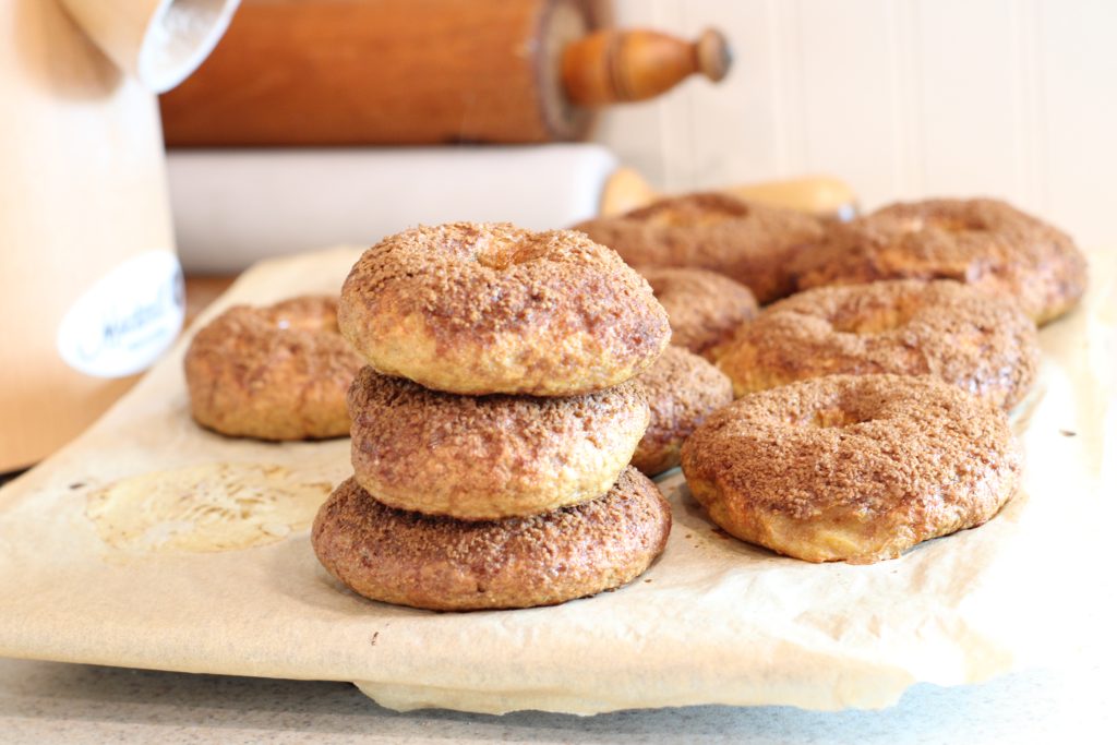 Easy homemade bagels with freshly milled flour setting on parchment paper on kitchen counter beside grain mill and rolling pins
