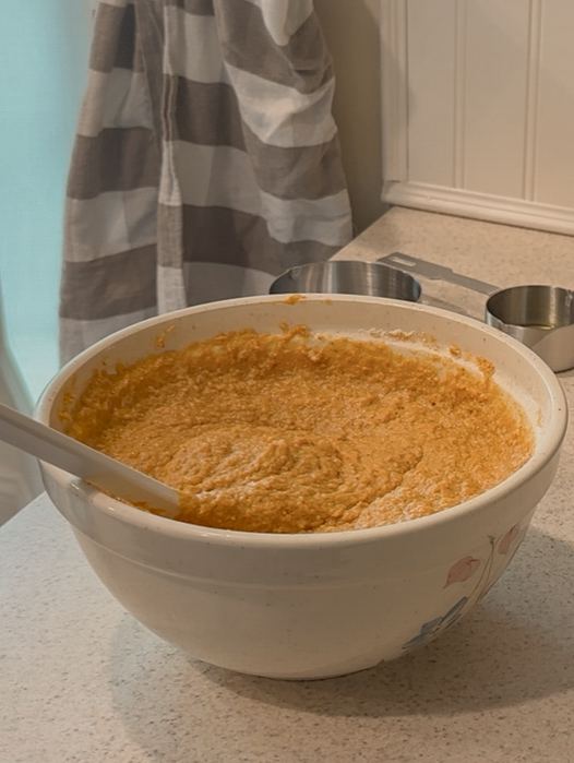 Pumpkin muffin batter in mixing bowl on counter beside measuring cups
