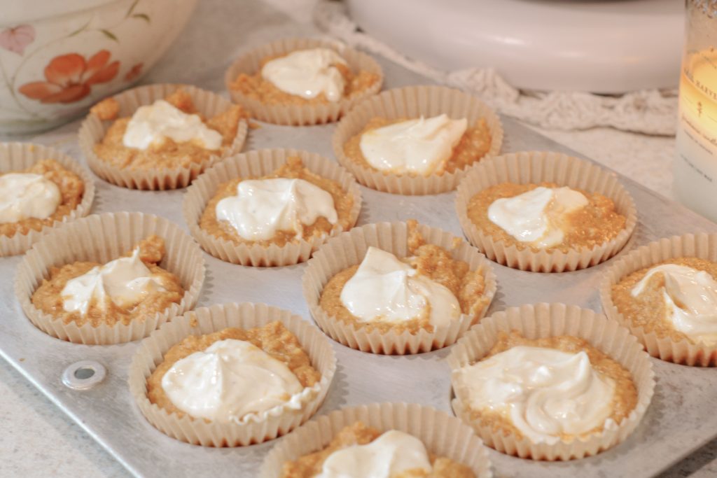 unbaked pumpkin muffins in tin setting on counter in front of lit candle and mixing bowl with flower