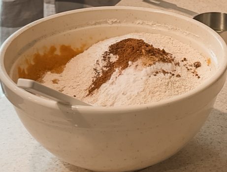 Ingredients for pumpkin muffins in mixing bowl on counter with measuring cup